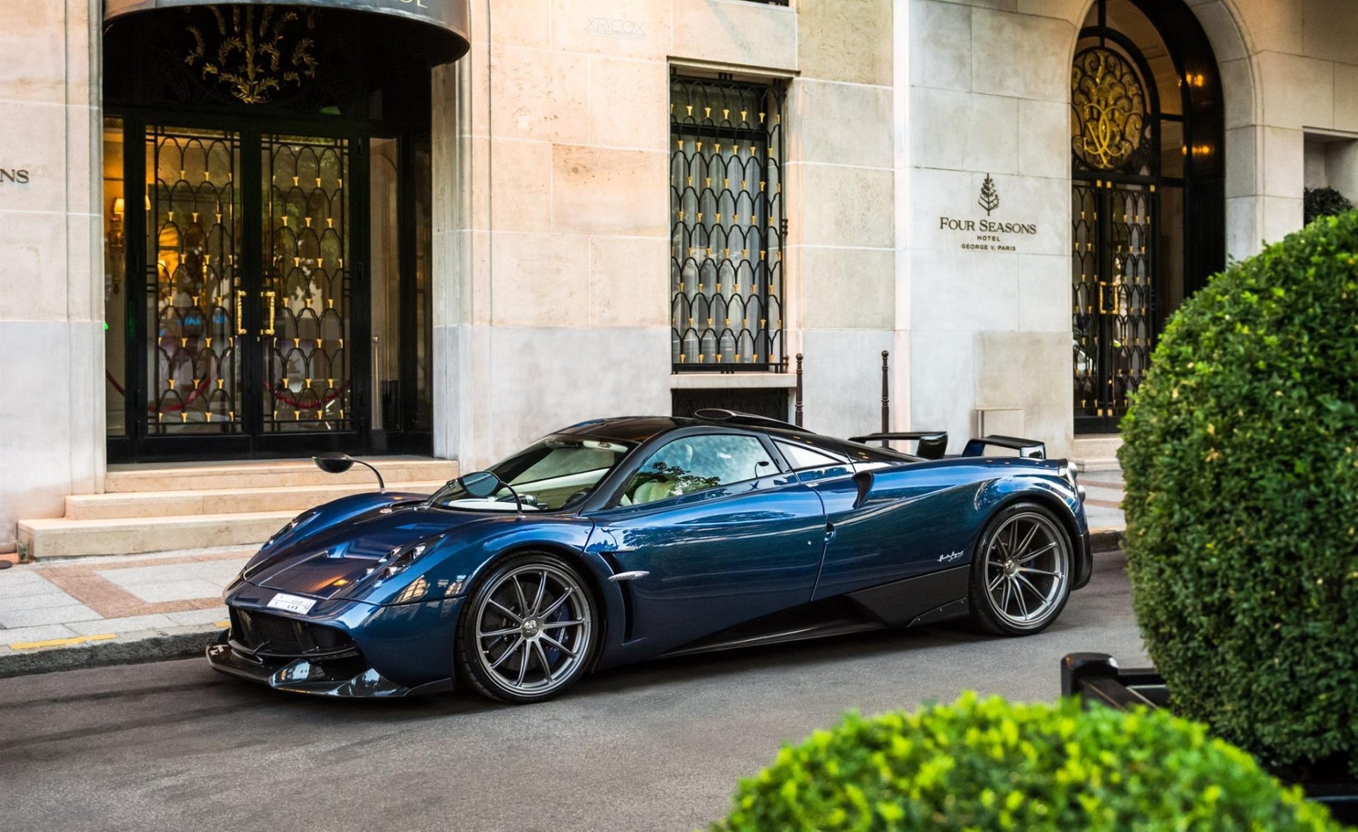 A sleek blue Pagani Huayra supercar parked outside an elegant building, captured in HD for a striking PC desktop wallpaper and background.