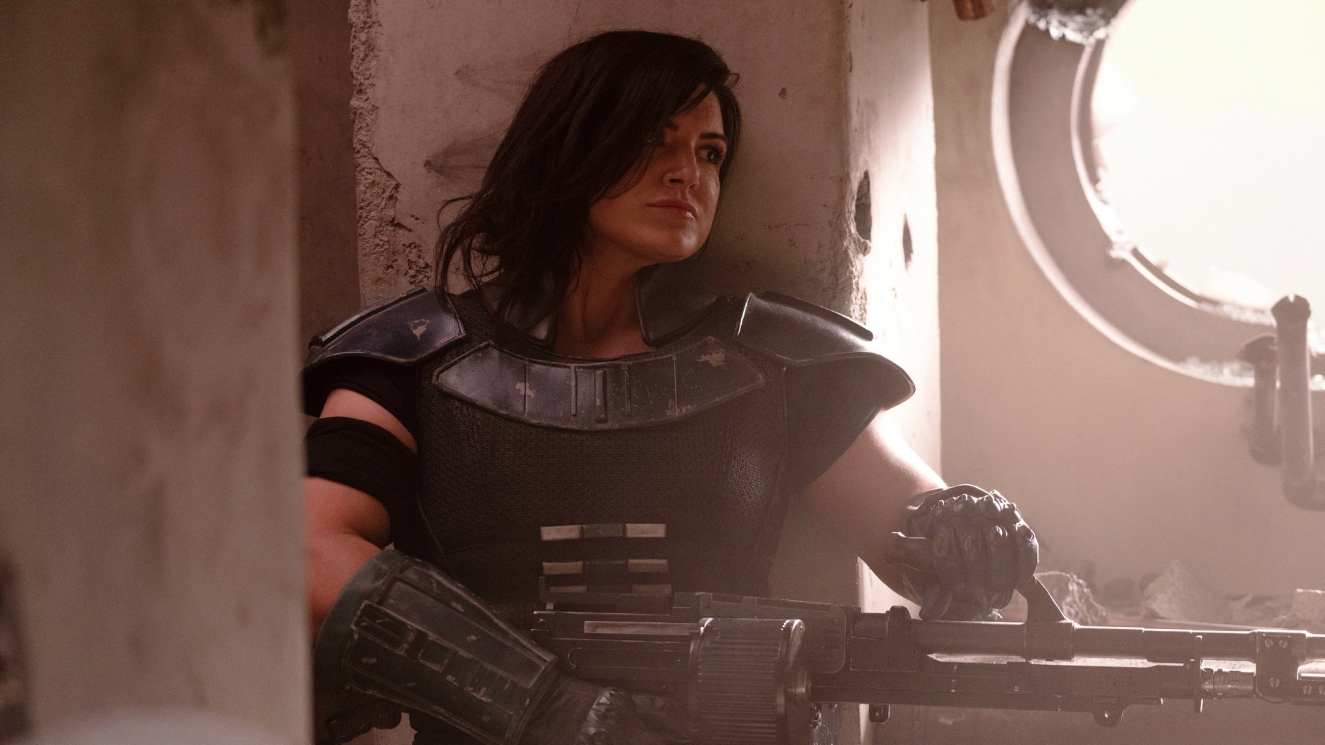 HD desktop wallpaper featuring Cara Dune, portrayed by Gina Carano, from the Star Wars TV show The Mandalorian, in a dimly lit setting holding a weapon.