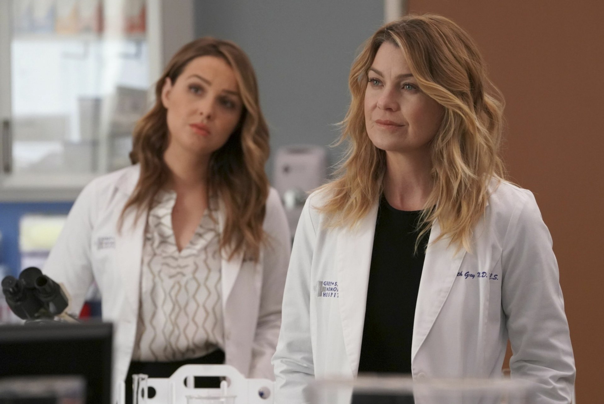 HD desktop wallpaper of two female characters from Grey's Anatomy in white lab coats, set in a medical environment.