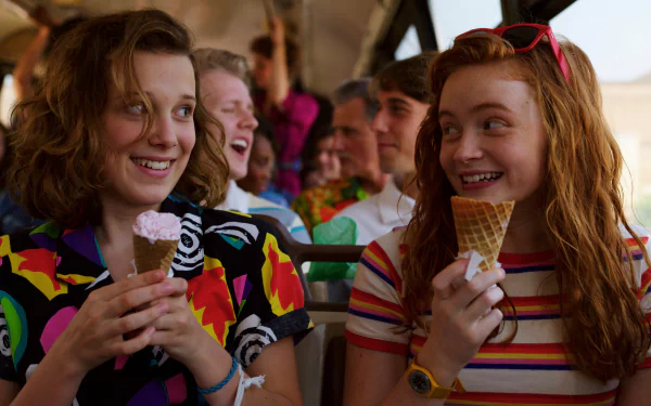 Millie Bobby Brown as Eleven and Sadie Sink as Max Mayfield from Stranger Things Season 3 enjoy ice cream together in this vibrant 4K Ultra HD TV show wallpaper.