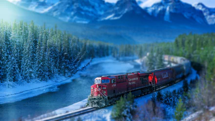 HD PC desktop wallpaper featuring a tilt-shift effect on a red locomotive train traveling through a snowy forest landscape with mountains in the background.