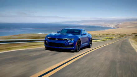A blue Chevrolet Camaro SS muscle car speeds along a coastal highway with ocean and cliffs in the background, captured in 4K Ultra HD for a PC desktop wallpaper.