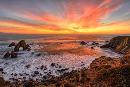 HD PC desktop wallpaper featuring a vibrant sunset over a rocky coastline with ocean waves gently washing ashore, highlighting nature's beauty.
