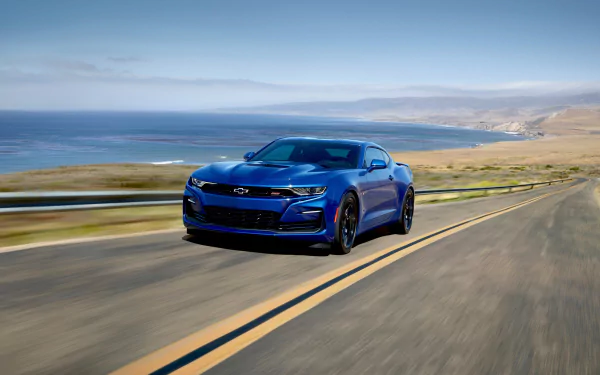 A blue Chevrolet Camaro SS muscle car speeds along a coastal highway with ocean and cliffs in the background, captured in 4K Ultra HD for a PC desktop wallpaper.