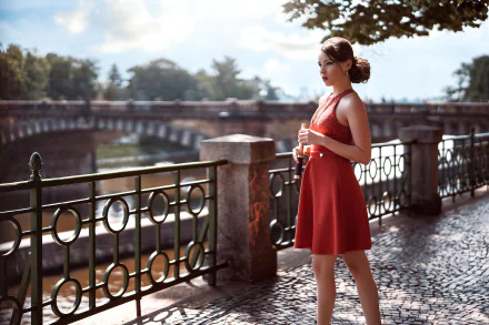 A brunette woman in a red dress stands by a riverside railing, with a blurred background enhancing the depth of field in this HD PC desktop wallpaper.