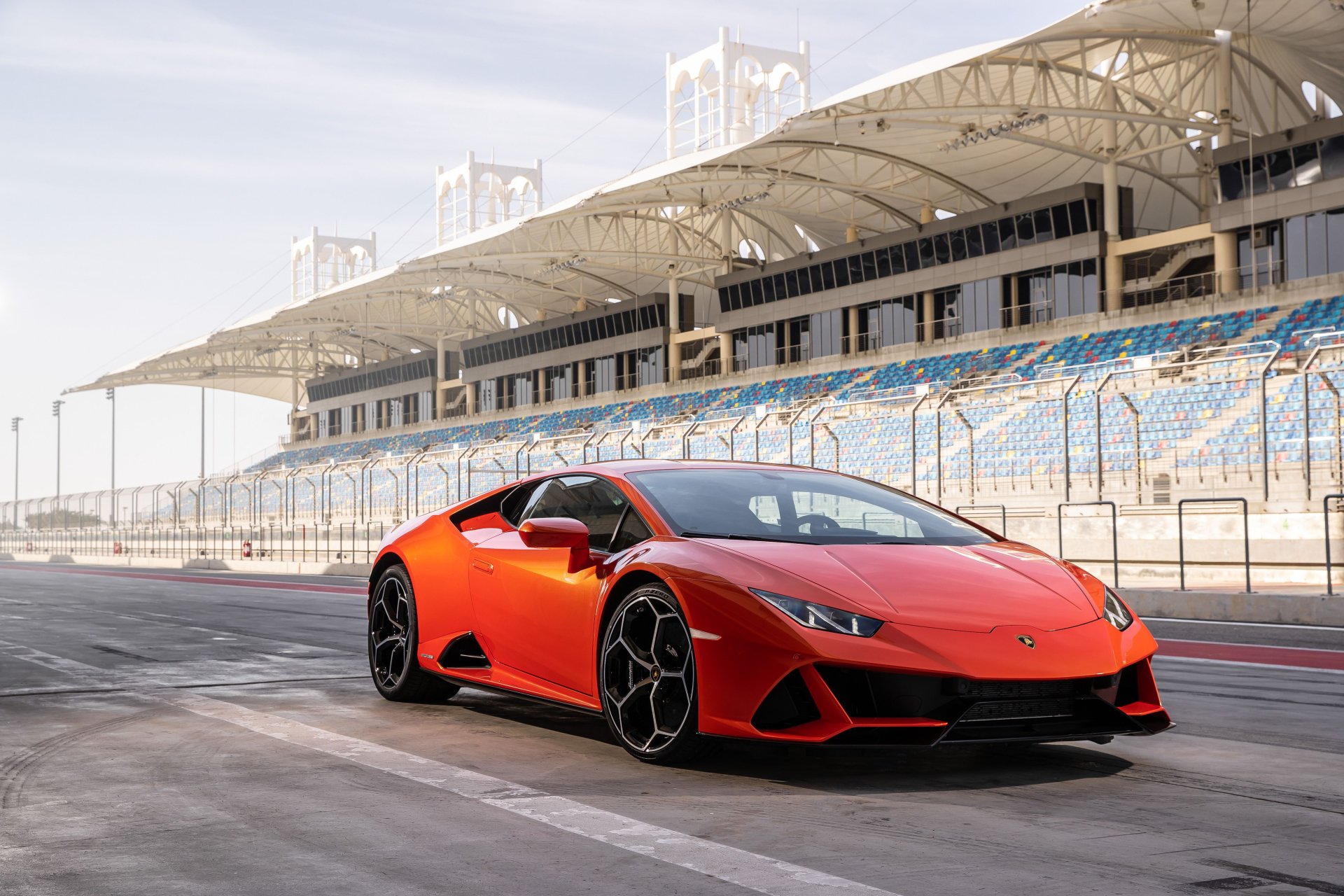 A vibrant orange Lamborghini Huracan Evo supercar parked on a racetrack with grandstands in the background, captured in crisp 4K Ultra HD quality.