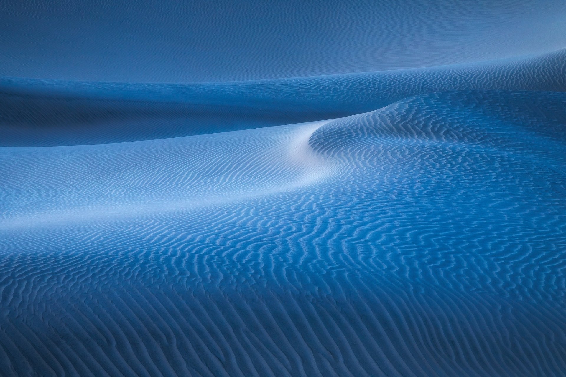 HD PC desktop wallpaper showcasing smooth, rippled sand dunes under soft blue lighting in a serene desert landscape.