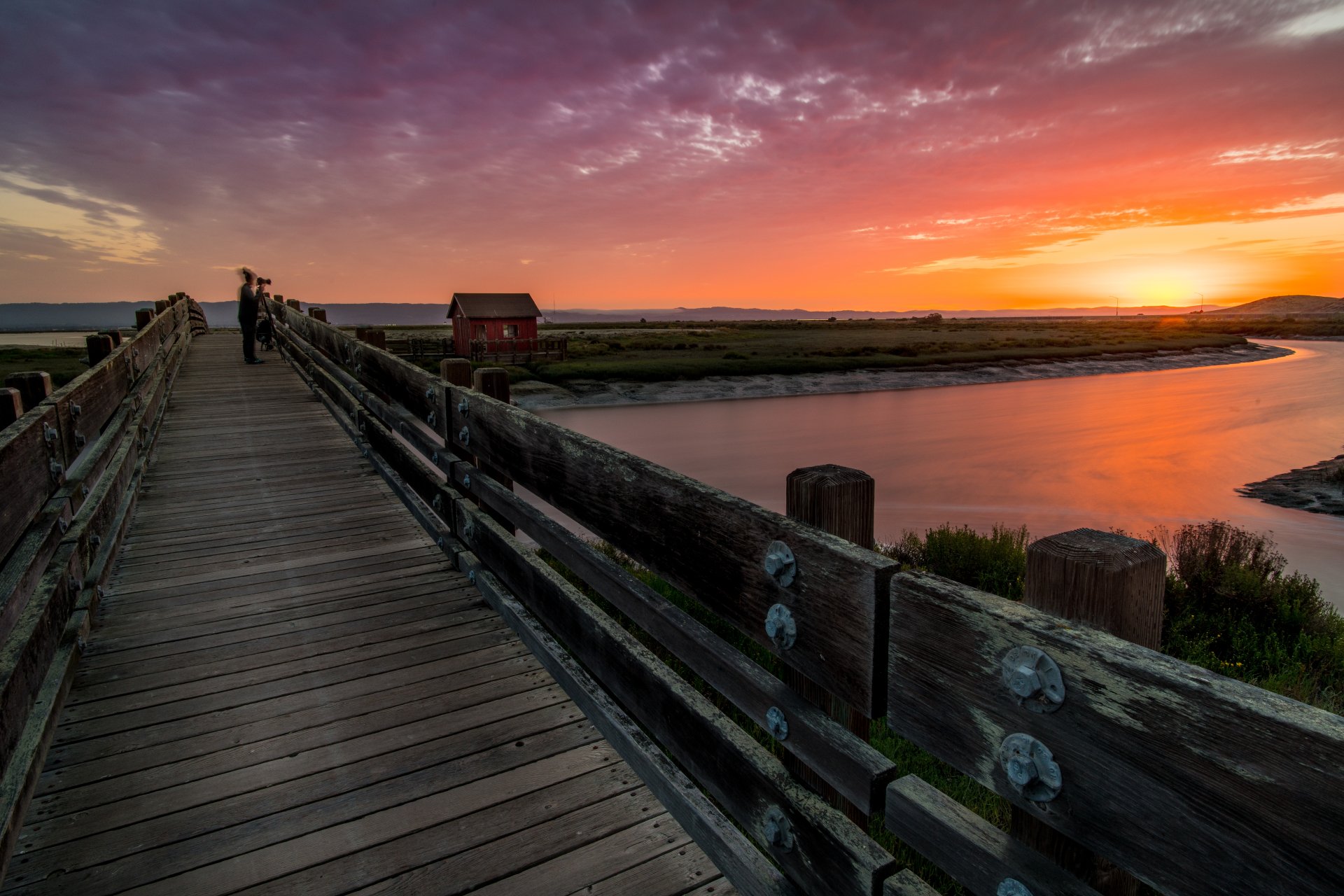 Sunset over a river with a wooden bridge and a cloudy sky, captured in stunning 8K Ultra HD photography for a vibrant PC desktop wallpaper.