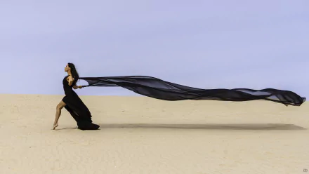 HD PC desktop wallpaper of a woman in a flowing black dress on sand, long sheer train billowing behind her, creating a dramatic, contemplative mood.
