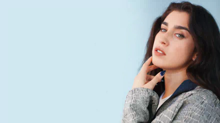 8K Ultra HD desktop wallpaper of an American singer: brunette with green eyes and bold lipstick, wearing a textured jacket and gazing off against a pale blue background.