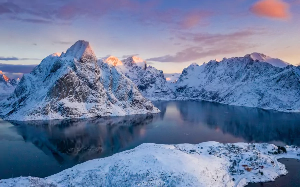 Winter scene of a snowy bay in Lofoten, Norway, with rugged mountains reflected in calm waters under a colorful sky. HD desktop wallpaper photography.