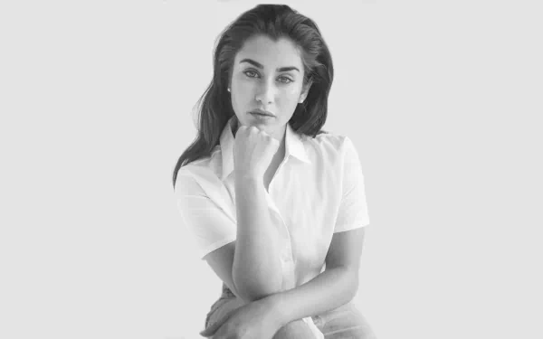 Monochrome 8K Ultra HD desktop wallpaper: portrait of an American singer seated with hand to chin, calm expression against a pale background.