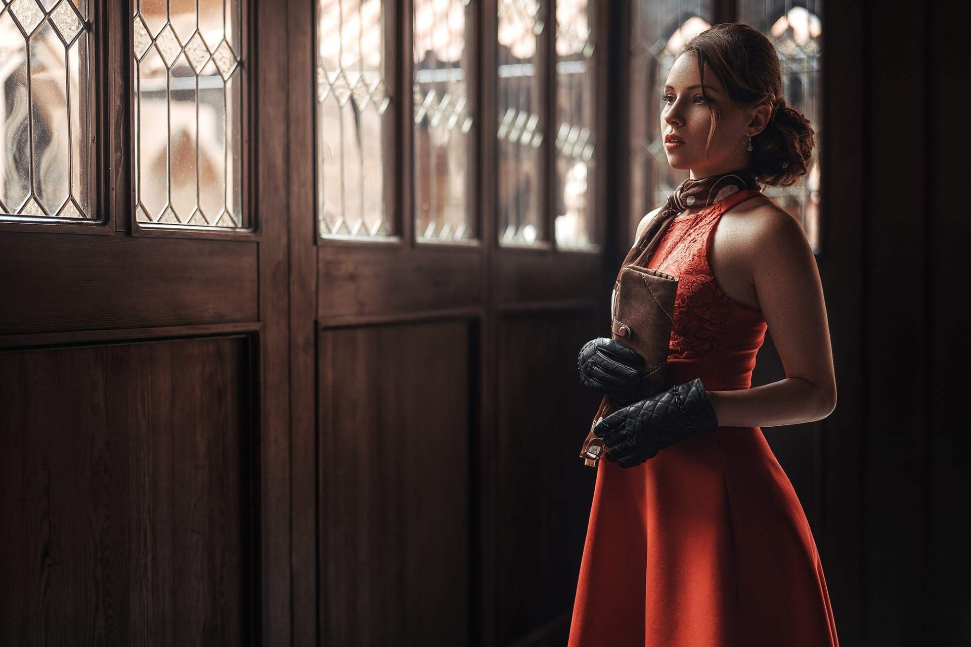 Brunette woman model in a red dress and black gloves stands by ornate wooden windows, captured in an elegant HD PC desktop wallpaper background.