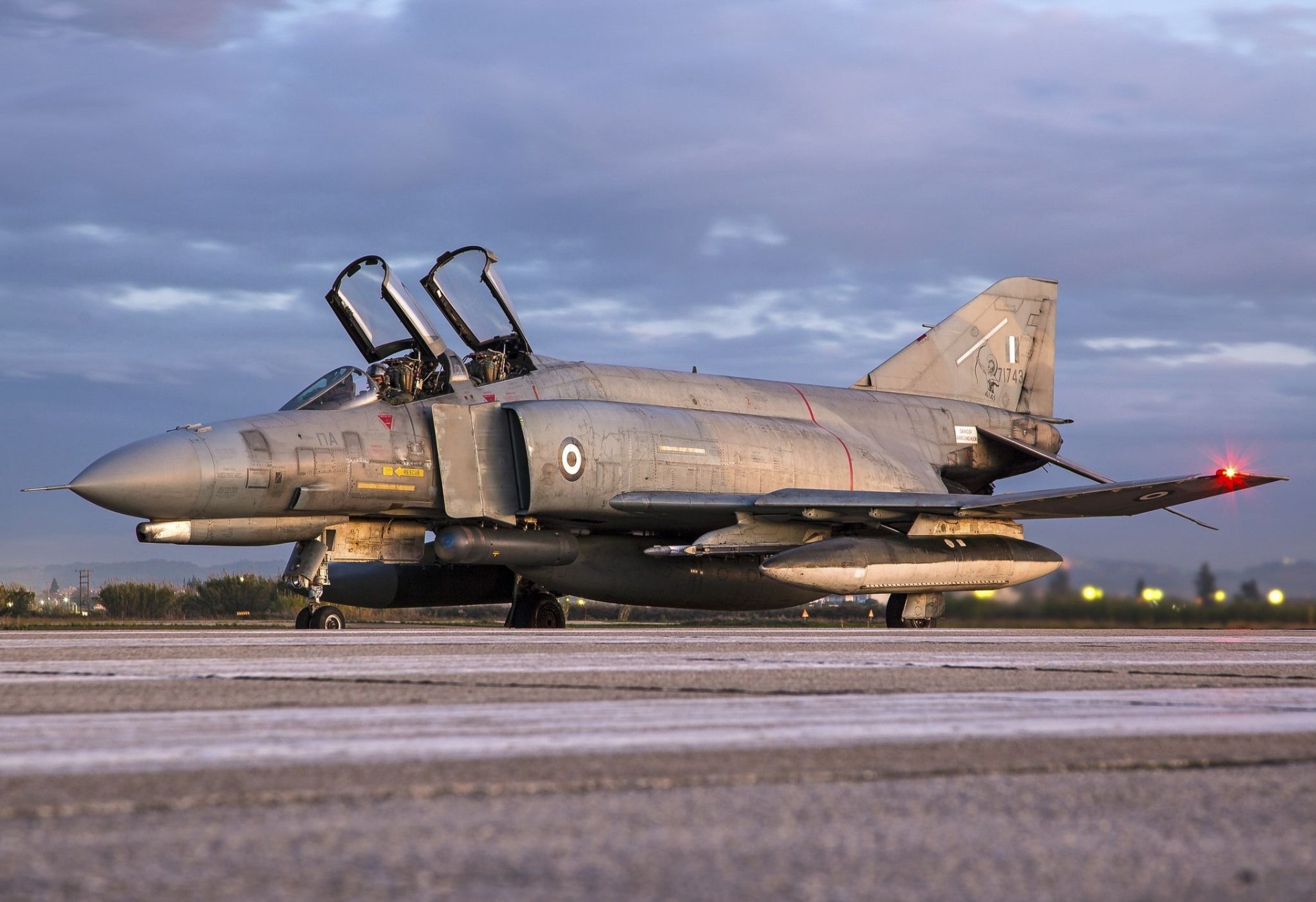 HD desktop wallpaper featuring a McDonnell Douglas F-4 Phantom II military jet fighter warplane on the runway under a cloudy sky.