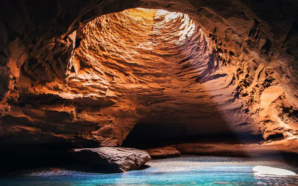 HD desktop wallpaper showing a stunning natural cave in Canada with sunlight streaming through the opening onto blue water inside.