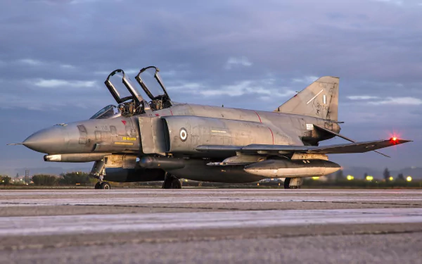 HD desktop wallpaper featuring a McDonnell Douglas F-4 Phantom II military jet fighter warplane on the runway under a cloudy sky.