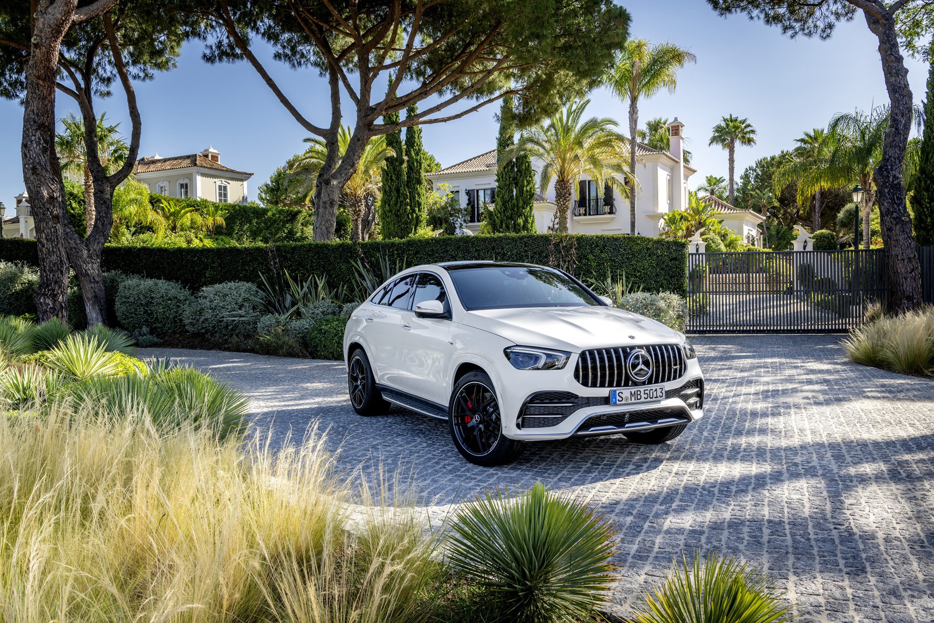 4K Ultra HD desktop wallpaper of a white Mercedes-AMG GLE 53 SUV (Mercedes-Benz) parked on a cobblestone drive before a gated villa with palm trees.