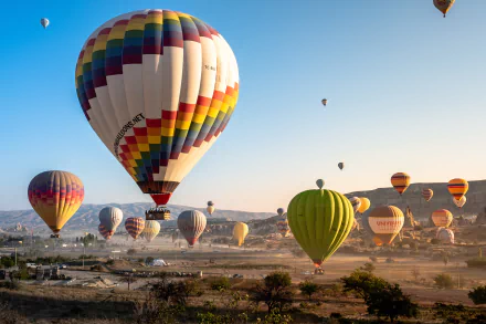 Colorful hot air balloons float over Cappadocia at sunrise, captured in stunning 4K Ultra HD as dawn light brightens the landscape with a vehicle visible below.