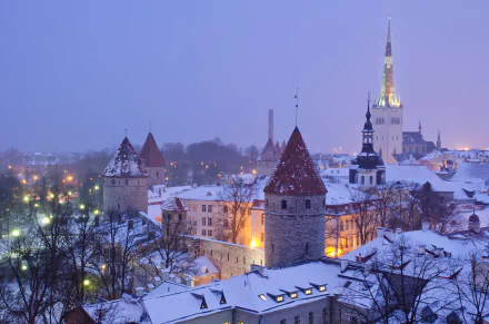 Snow-covered rooftops and historic buildings of Tallinn glow warmly under dusk light in this 4K Ultra HD winter cityscape wallpaper.