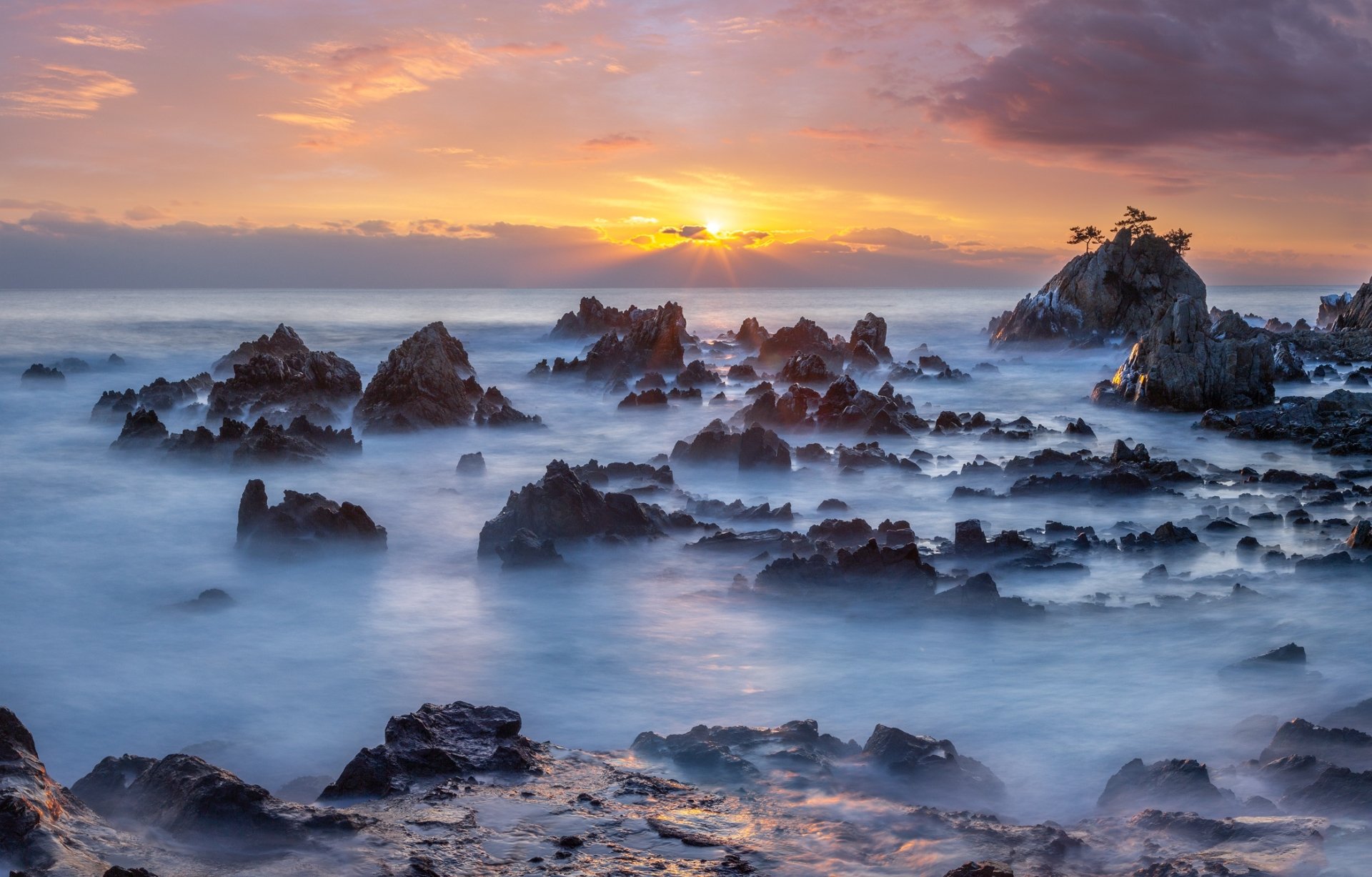 HD desktop wallpaper of a South Korean ocean sunrise with rocky formations along the horizon under a vibrant, colorful sky.