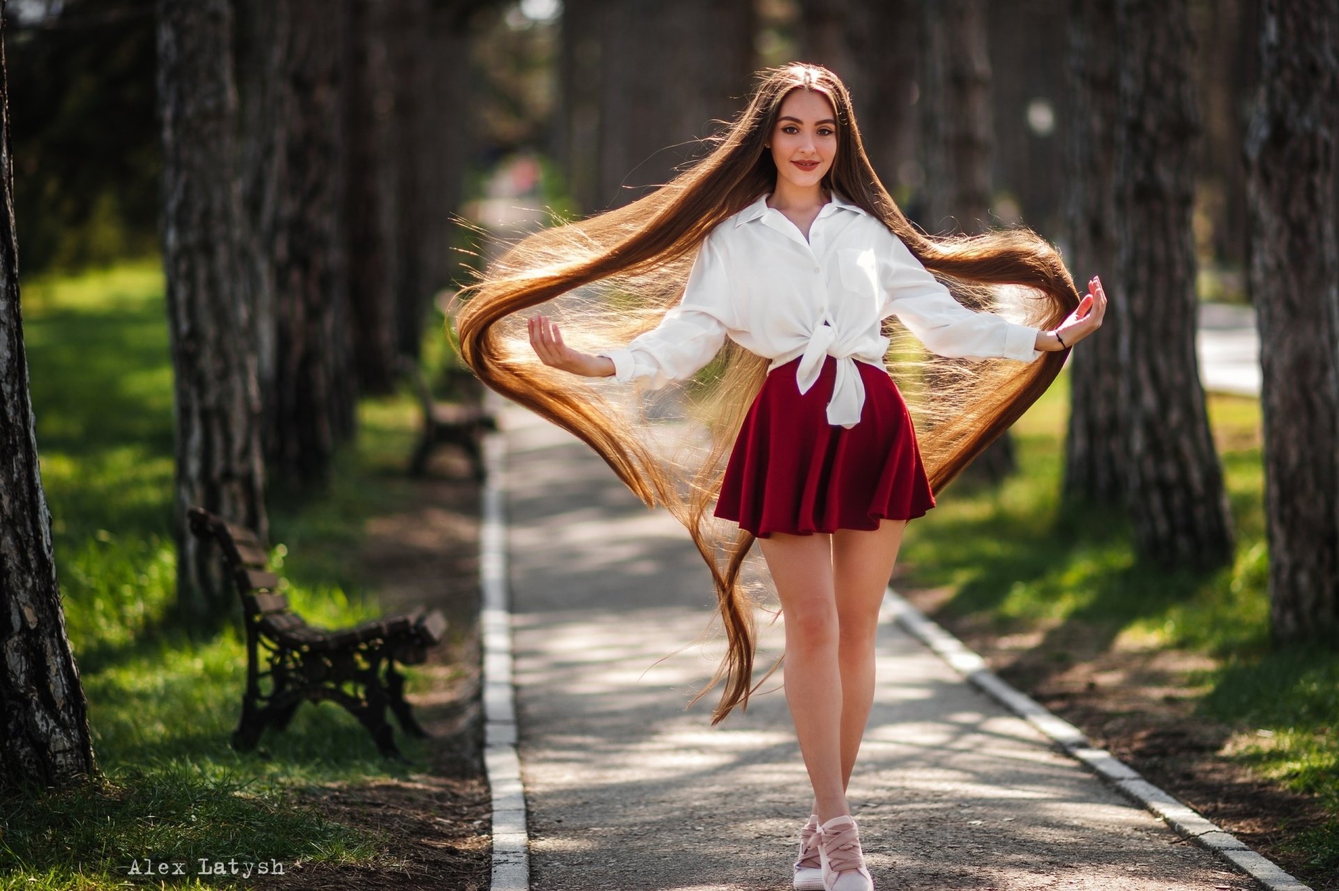 A redhead woman model with long hair and a red skirt poses along a tree-lined path, captured with a shallow depth of field in this HD desktop wallpaper.