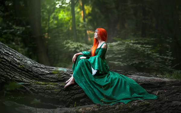 A model with vibrant orange hair wearing a flowing green dress poses in cosplay while seated on a large tree trunk in a serene forest, captured in HD for a PC desktop wallpaper.
