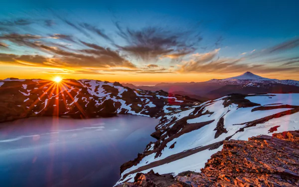 2K Quad HD PC desktop wallpaper of a snowy mountain landscape: sunrise over a snow-covered crater lake, vivid sky, sunburst and rugged nature.