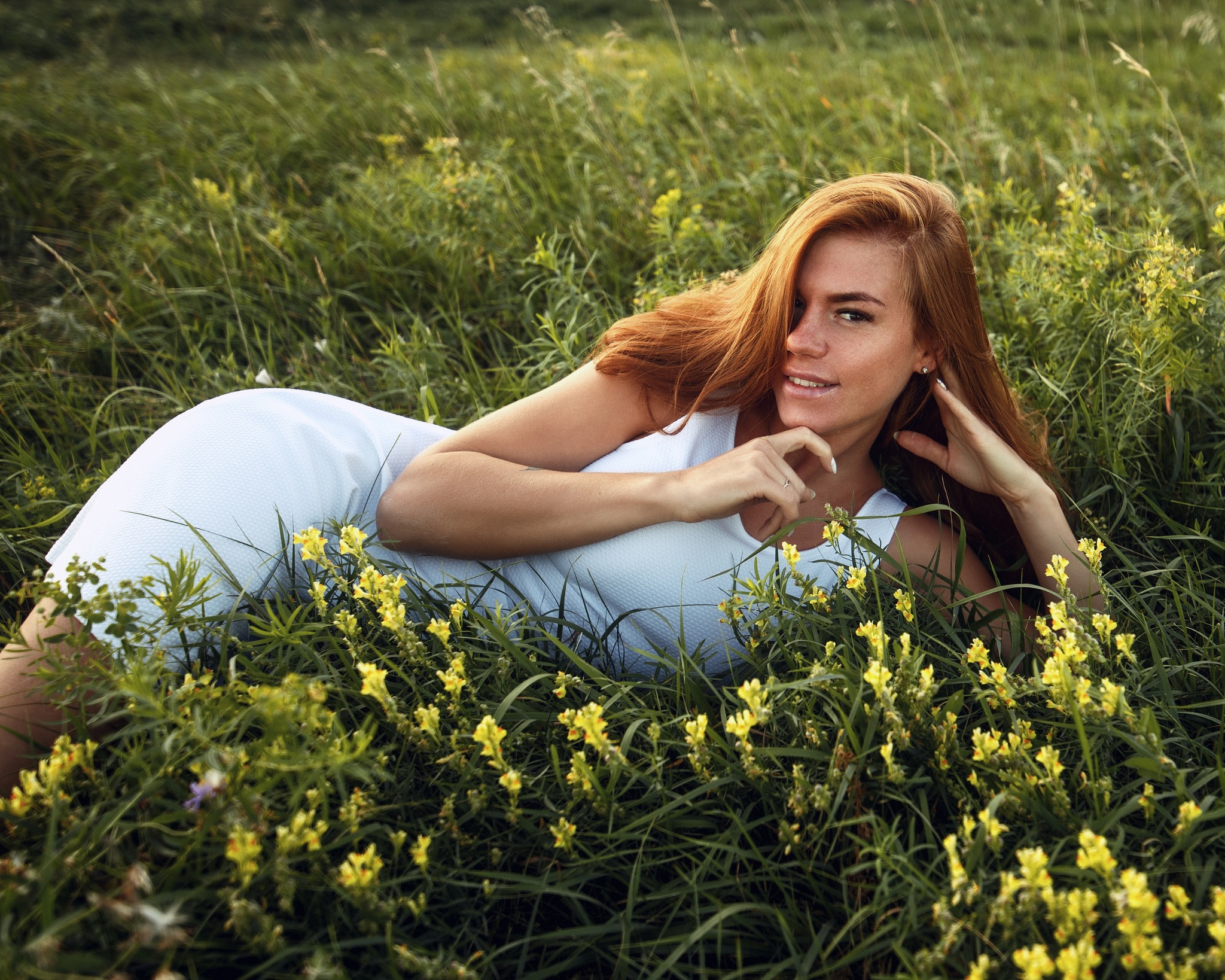Обои на стол женщины. Рыжая девушка в траве. Девушка с длинными волосами лежит на траве с цветами. Улыбка природы.