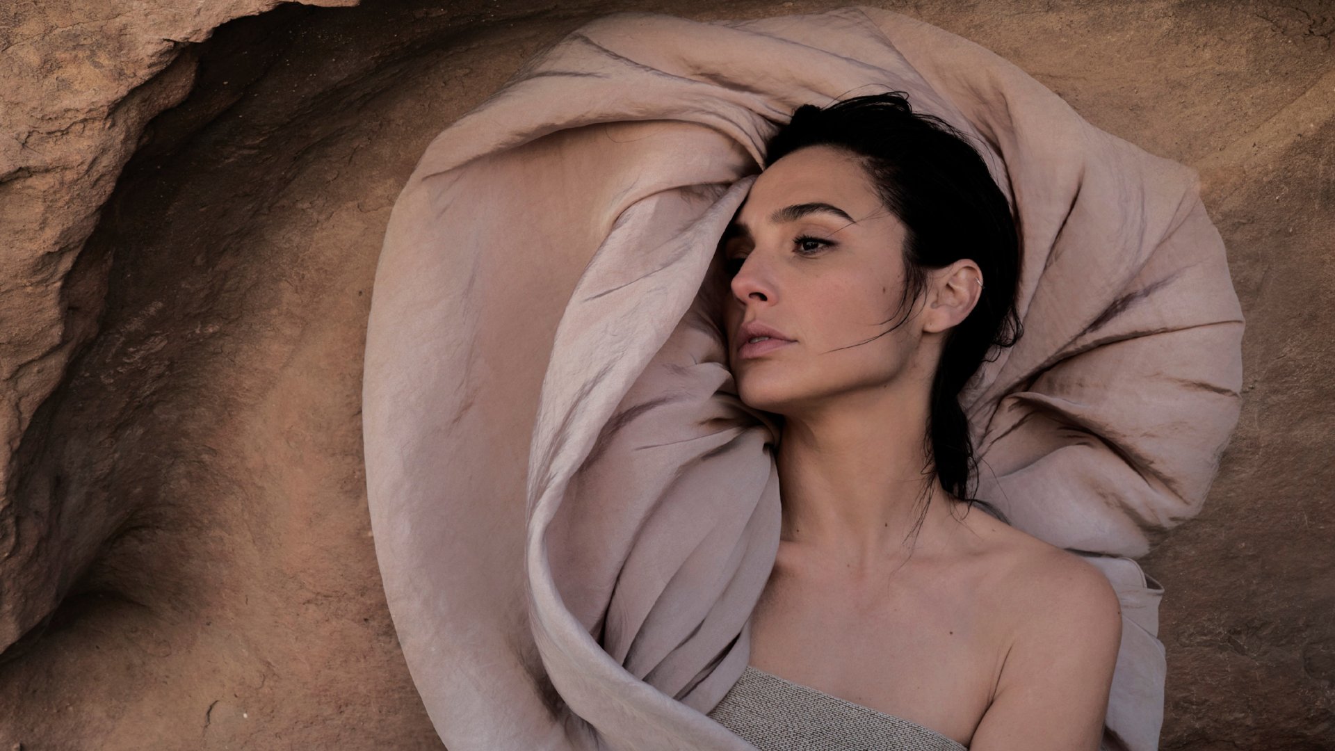 HD desktop wallpaper featuring Israeli model and actress with black hair lying down against a textured background, showcasing a calm and elegant pose.