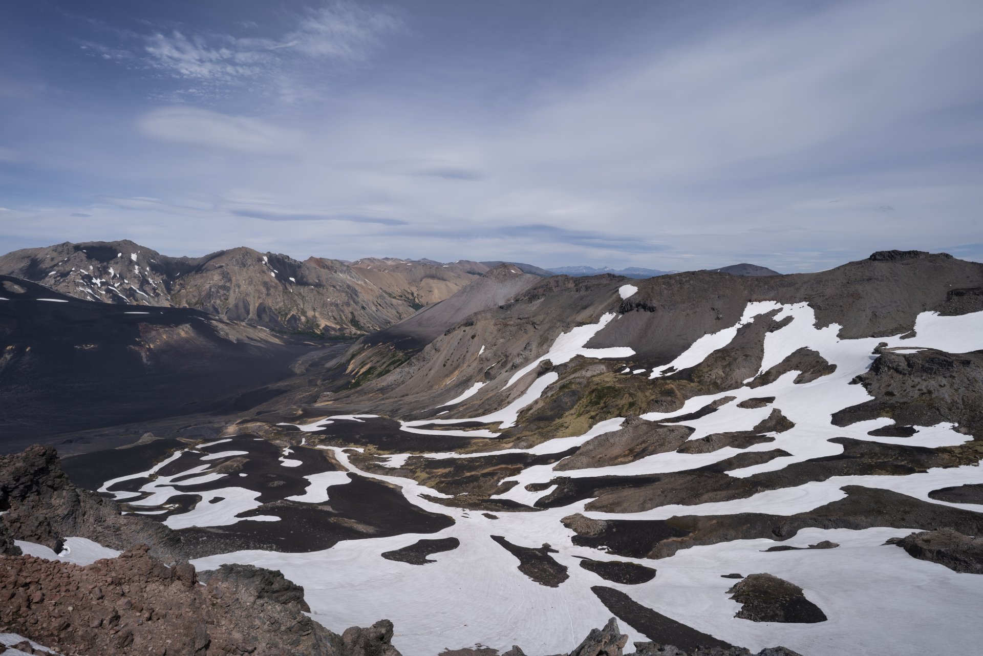 8K Ultra HD PC desktop background: volcanic rock nature landscape with dark lava fields and scattered snow patches under a wide cloudy sky.