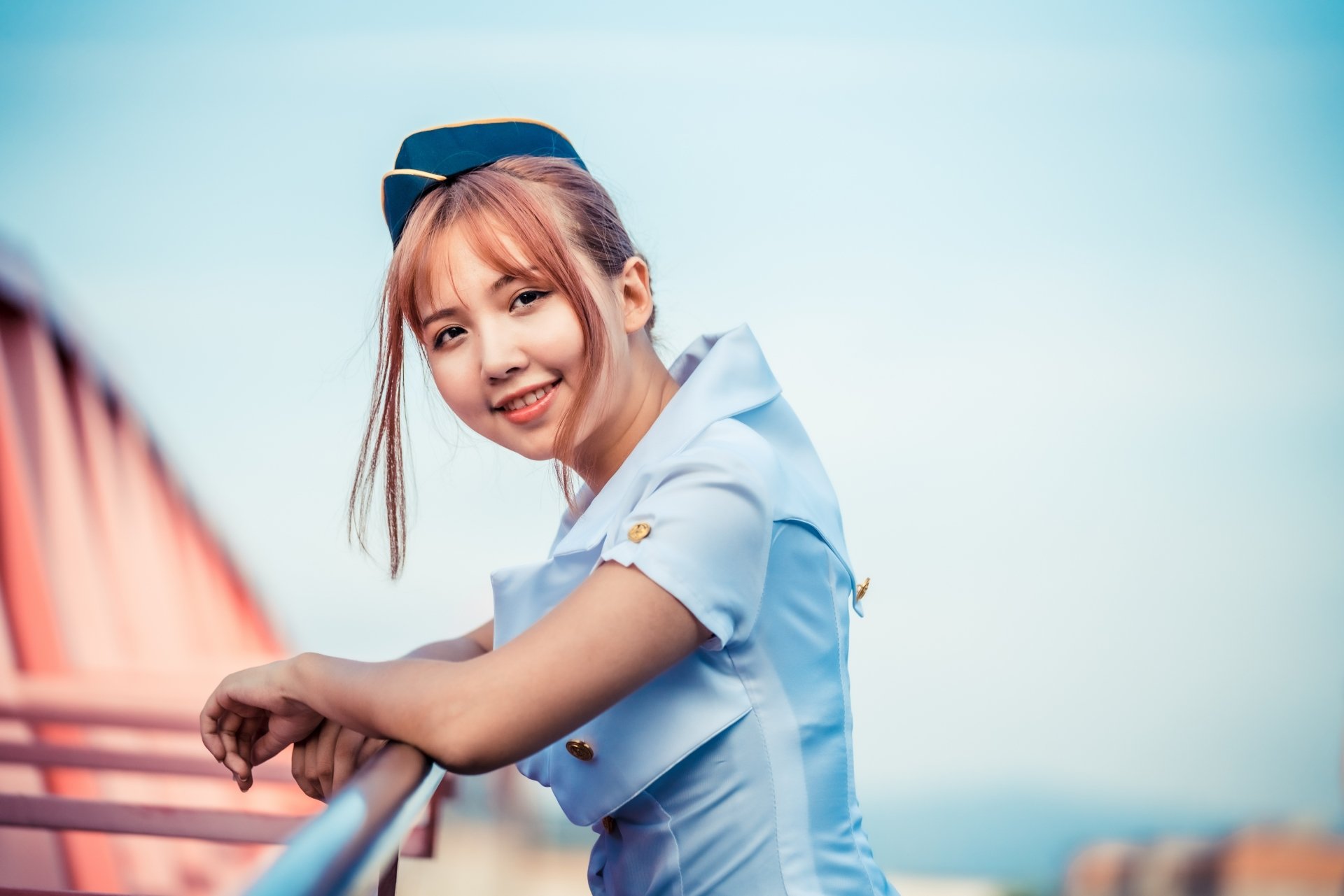 Brunette Asian stewardess in uniform smiling, photographed with depth of field effect, featured as a 4K Ultra HD desktop wallpaper and background.