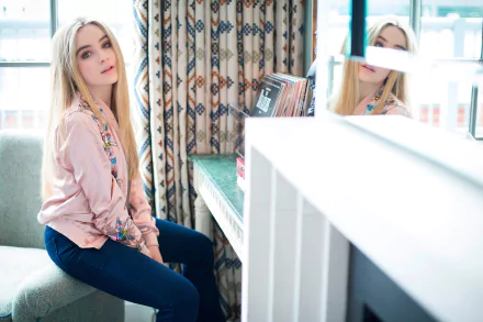 4K Ultra HD desktop wallpaper: long-haired blonde woman in a pink jacket and jeans seated by a window with a mirror reflection, relaxed music‑artist atmosphere.