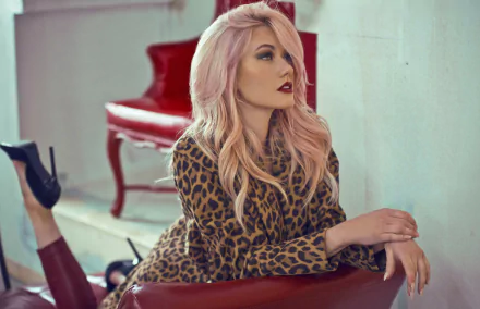 4K Ultra HD wallpaper of American actress Katherine McNamara with pink hair and bold lipstick, lounging on a red leather couch in a leopard print outfit.