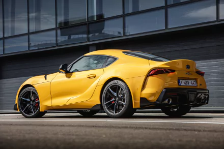 HD desktop wallpaper featuring a sleek yellow Toyota GR Supra parked in an urban setting, showcasing its sporty design and modern aesthetics.