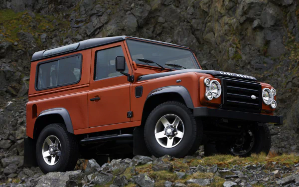Orange Land Rover Defender SUV parked on rocky terrain, showcased in a sharp 4K Ultra HD desktop wallpaper background.