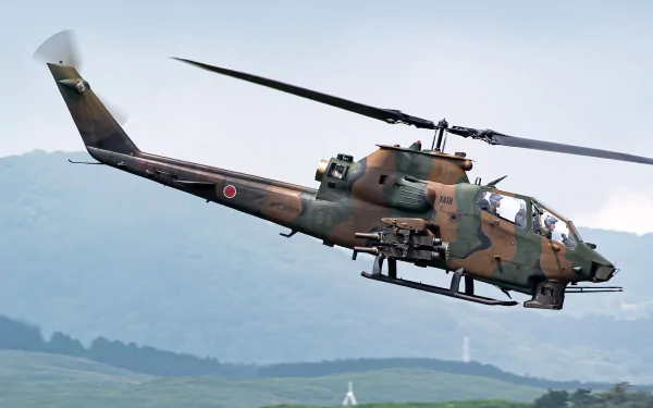 HD PC desktop wallpaper: camouflaged Bell AH-1 Cobra military attack helicopter in flight over rolling green hills.