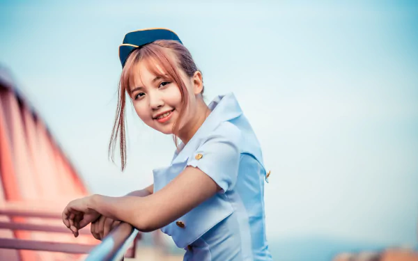 Brunette Asian stewardess in uniform smiling, photographed with depth of field effect, featured as a 4K Ultra HD desktop wallpaper and background.