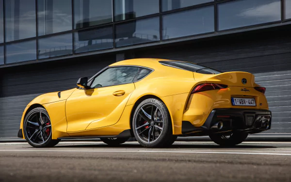 HD desktop wallpaper featuring a sleek yellow Toyota GR Supra parked in an urban setting, showcasing its sporty design and modern aesthetics.