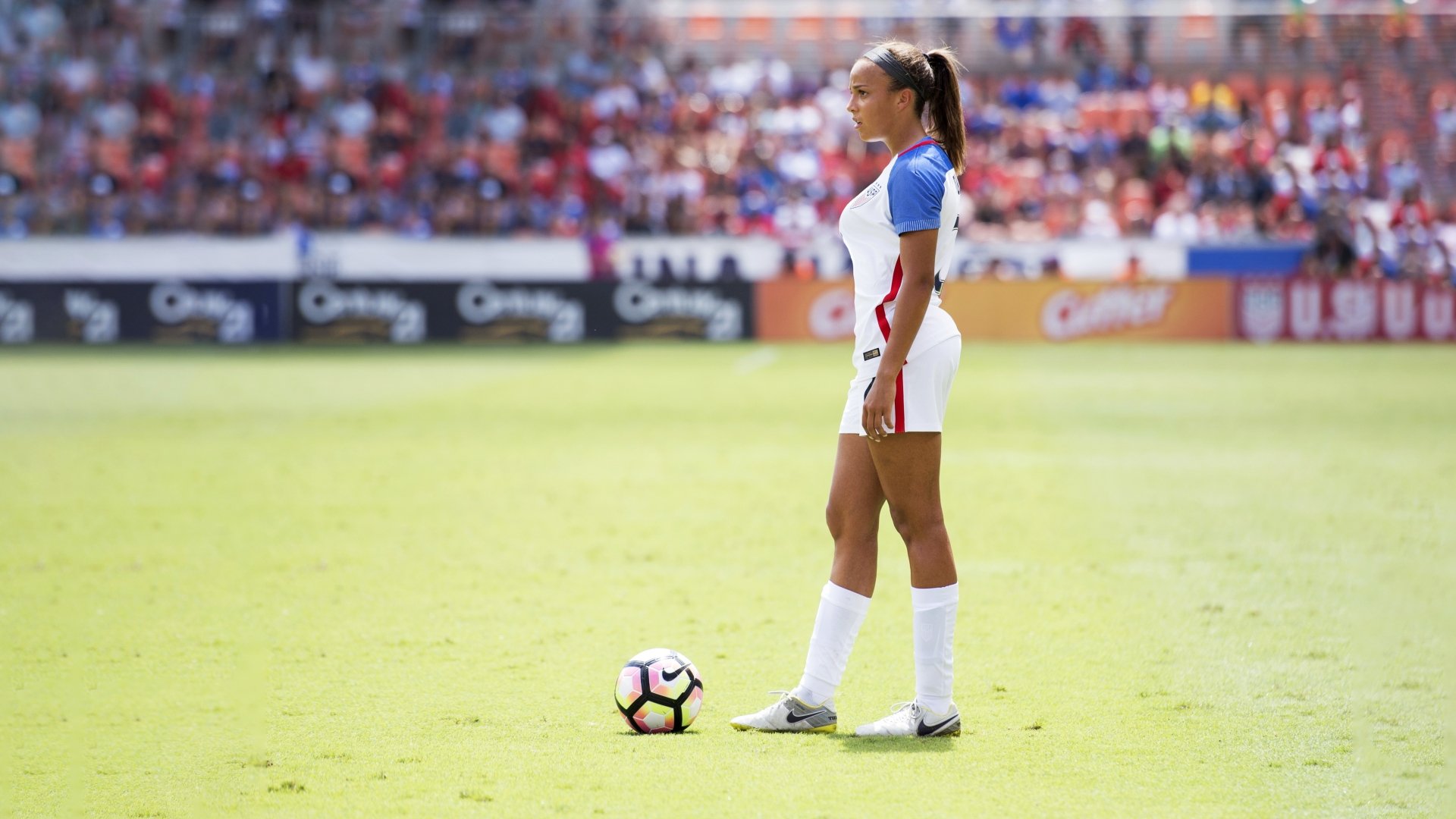 A female soccer player standing on a grassy field with a ball at her feet, captured in a 4K Ultra HD PC desktop wallpaper showcasing sports and legs.