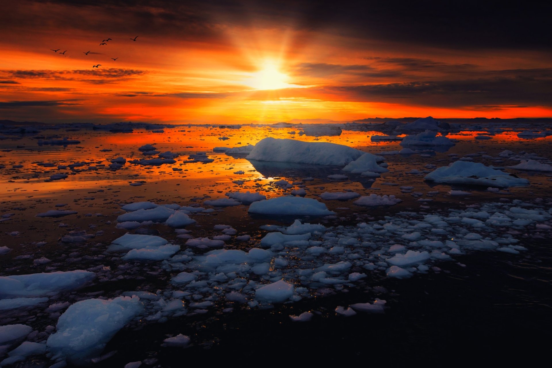 HD PC desktop wallpaper and background: nature scene of a blazing sunset over icy waters, a lone iceberg and scattered sea ice reflecting warm orange and red light.