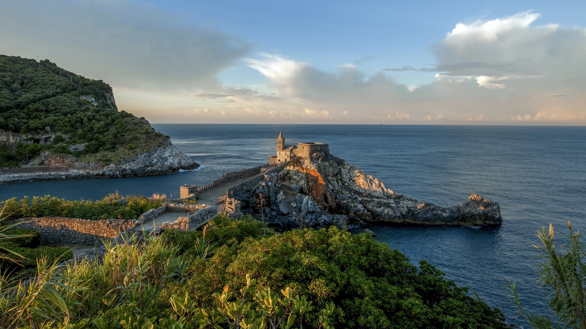 4K Ultra HD desktop wallpaper featuring a serene coastal church perched on rocky cliffs, surrounded by lush greenery and calm ocean waters under a partly cloudy sky.
