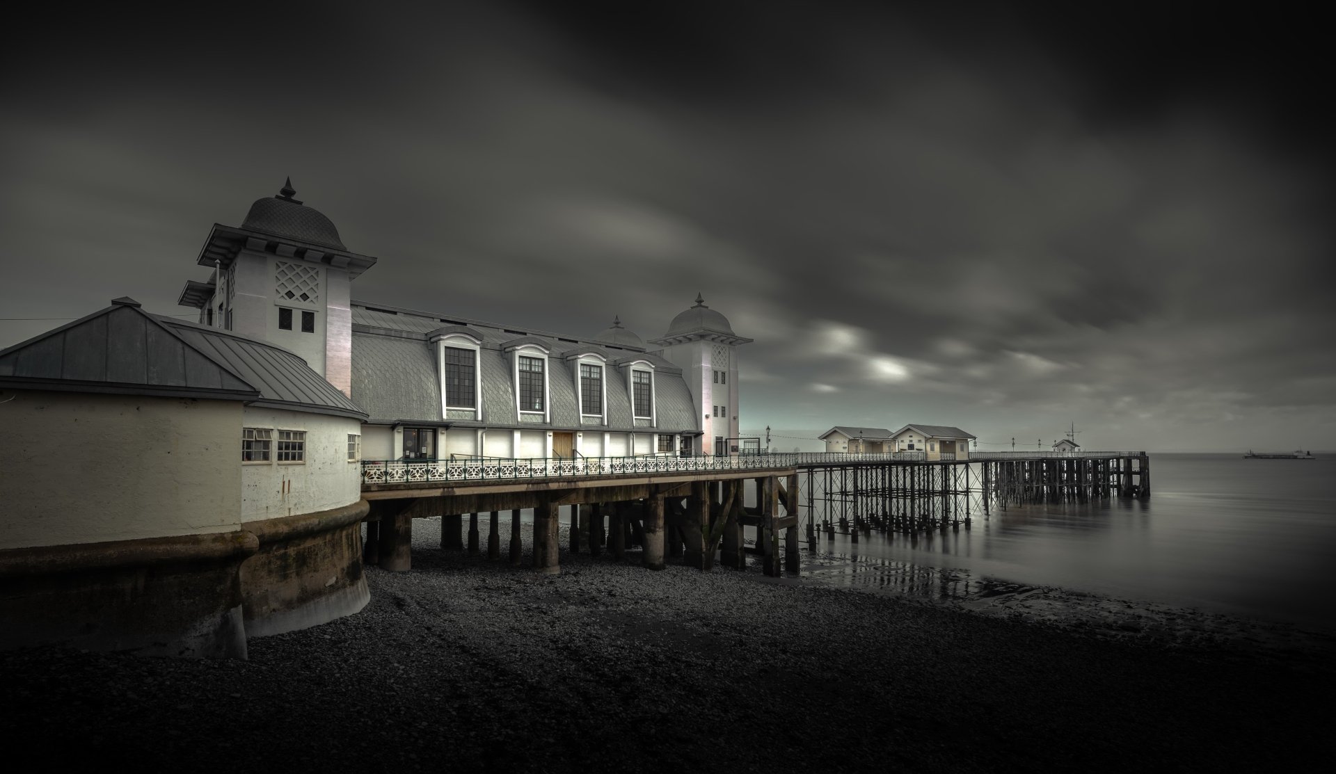 A black and white 4K Ultra HD image of a man-made pier extending into calm waters under a cloudy sky.