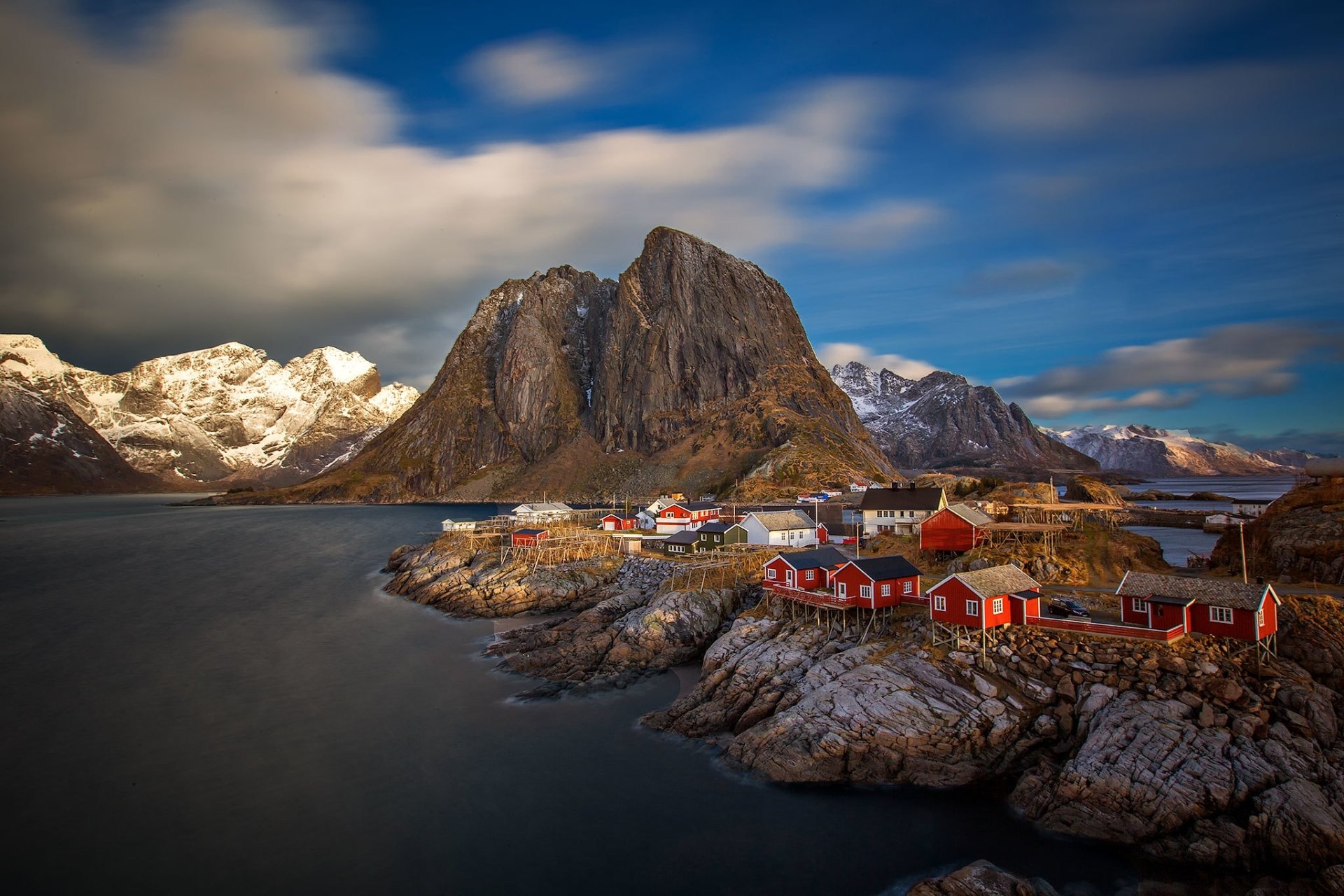 Reine, Lofoten, Norway — red fishing houses on rocky islets by the sea under dramatic clouds. HD PC desktop wallpaper photography.