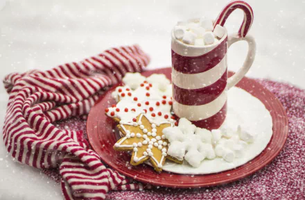 HD desktop wallpaper of a festive scene with a striped mug of hot chocolate, a candy cane, and assorted holiday cookies on a red plate, set against a snowy background. Christmas decorations enhance the holiday spirit.