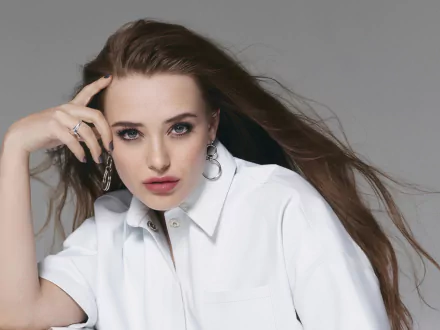 Close-up of Australian actress Katherine Langford with blue eyes and brunette hair, wearing a white shirt against a gray background, shown as an HD desktop wallpaper.
