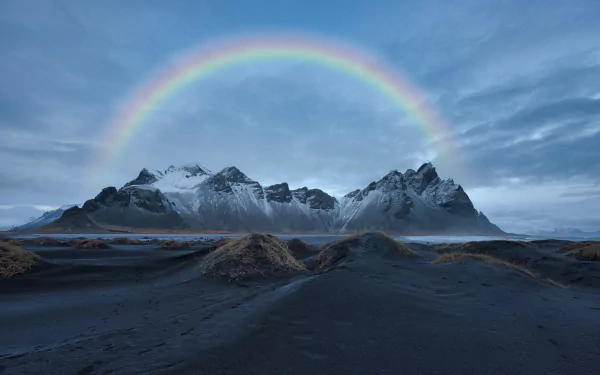 Vestrahorn Mountain in Iceland rises behind a black sand beach under a vibrant rainbow, captured in stunning 8K Ultra HD detail.