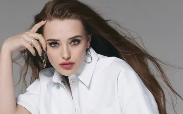 Close-up of Australian actress Katherine Langford with blue eyes and brunette hair, wearing a white shirt against a gray background, shown as an HD desktop wallpaper.