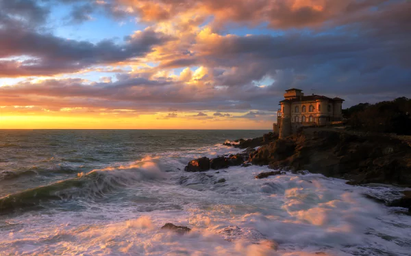 Castello del Boccale, a man-made structure, stands on the rocky coast of Tuscany, Italy, with waves crashing under a dramatic sunset sky in this 4K Ultra HD wallpaper.