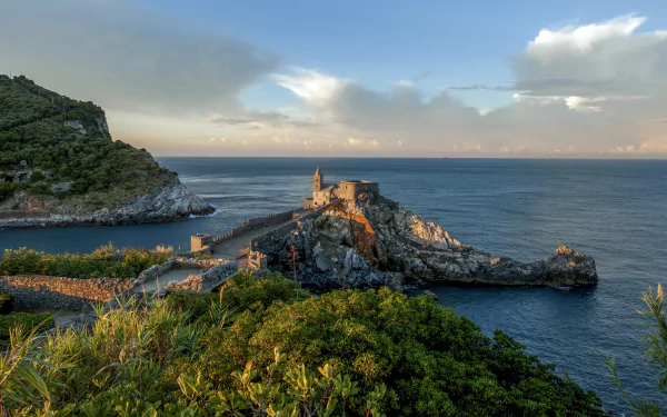 4K Ultra HD desktop wallpaper featuring a serene coastal church perched on rocky cliffs, surrounded by lush greenery and calm ocean waters under a partly cloudy sky.