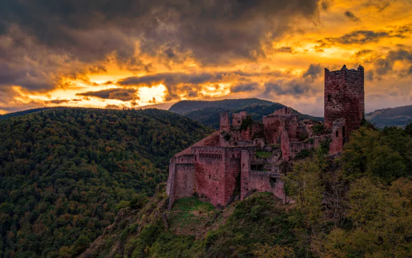 4K Ultra HD image of a man-made ruined castle perched on a forested hill in France under a fiery sunset sky.